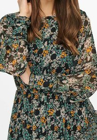 Multikleurige jurk met bloemen- en stippenpatroon van doorzichtig materiaal, met lange mouwen en gerimpelde manchetjes, met een getailleerde taille-omschrijving.