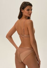 Nacktes zweiteiliges Lingerie-Set mit transparenten und soliden Stoffabschnitten, dünnen verstellbaren Trägern und Haken- und Ösenverschluss auf der Rückseite. Glatte Textur.