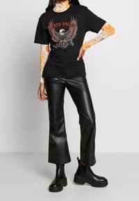 Sort grafisk t-shirt med ørnerdesign og "Death Valley" tekst, lagd over en marmor orange langærmet top. Kombineret med sorte faux læderbukser og kraftige støvler.
