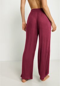 Pantalones amplios y fluidos en un tono burdeos profundo con una cintura elástica. Hechos de una tela suave y texturada; el diseño presenta un ajuste holgado y piernas de largo completo.