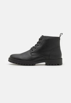 Bottines noires en cuir avec un devant à lacets, bout arrondi et semelle en caoutchouc robuste. Équipées d'une languette à l'arrière pour un enfilage facile.