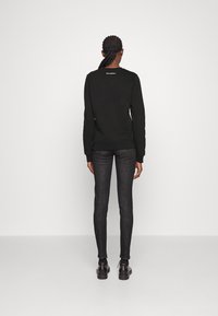 Svart sweatshirt med långa ärmar och ribbade ärmslut, kombinerad med mörka denimjeans. Enkel design, inga framträdande mönster eller accenter.