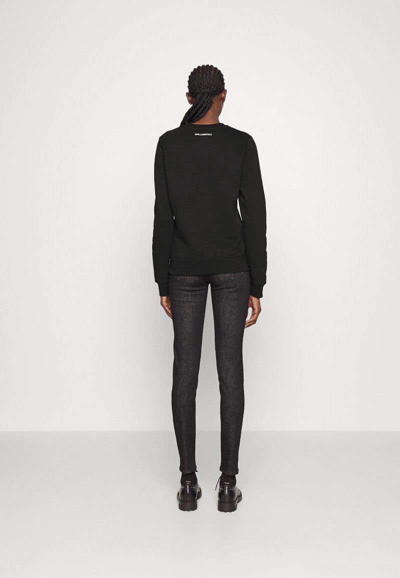 Svart sweatshirt med långa ärmar och ribbade ärmslut, kombinerad med mörka denimjeans. Enkel design, inga framträdande mönster eller accenter.