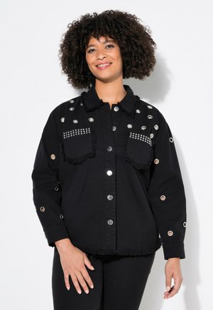 Veste en denim noir avec des fermetures à boutons argentés, accents de franges et clous sur les poches avant et les manches. Présente des œillets sur les manches.