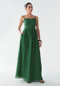 Maxi-Kleid aus strukturiertem dunkelgrünem Stoff, mit dünnen Trägern und einem taillierten Oberteil mit geraffter Taille, Taschen und gewelltem Saum.