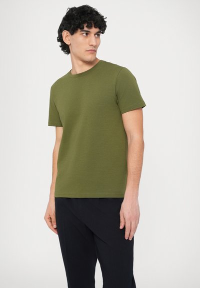 Λαδί πράσινο, κοντομάνικο μπλουζάκι από ομαλή ύφανση. Απλός σχεδιασμός με στρογγυλή λαιμόκοψη, εφαρμοστή γραμμή, συνδυασμένο με σκούρο υφασμάτινο παντελόνι με υφή.