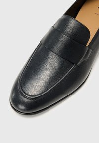 Black leather loafers with a textured finish, a smooth band across the vamp, and a rounded toe. The interior is tan.