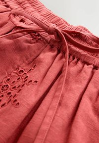 Karmosinrødt tekstureret stof med elastisk taljebånd og bindebånd. Har delikate broderiaccents i et blomstermønster på siden.