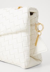 Vitt vävt skinnclutch med vikbar lock, guldkedja och triangulär läderetikett med guldmetallaccent.