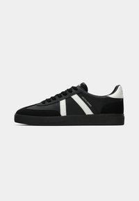 Black low-top sneaker with white stripes, black laces, textured black sole, and white heel accent, branded "JACK & JONES" on side.