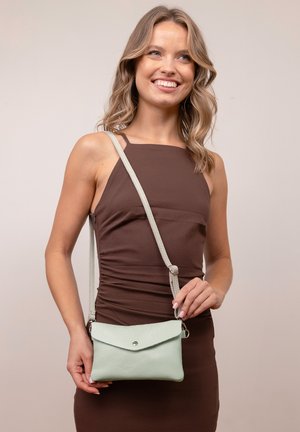 Mint green leather crossbody bag with a flap closure, textured surface, and adjustable strap. Model holds the bag against a neutral background.