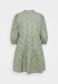 Ljusgrön klänning med puffärmar, ett lagerat fåll och blommönstrad hålmönstring. Har en krage och knappstängning bak.