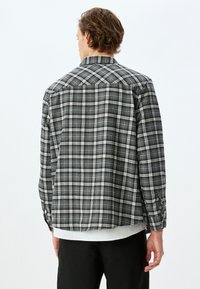 Sorte og hvide ternet skjorte med lange ærmer, knappede manchetter og rygdetaljer. Fremstillet af et letvægtsstof.