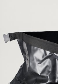 Saco preto impermeável com superfície texturizada, ampla alça em tecido com fivela e parte superior aberta. Projetado para durabilidade e utilidade.