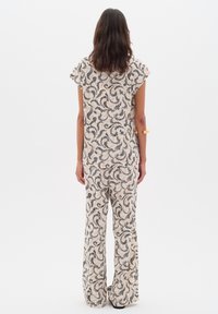 Completo a due pezzi composto da un top a maniche corte e pantaloni larghi in un tessuto color crema con motivi paisley neri a spirale.