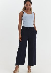 Navy wide-leg trousers with a drawstring waistband and side pockets, made from a smooth fabric. Paired with a light blue tank top.