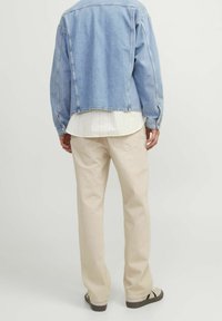 Džísková bunda v světle modré, krátký střih; spárovaná s bílou, texturovanou košilí a béžovými, volně padnoucími kalhotami. Viditelné jednoduché, pohodlné obuv.