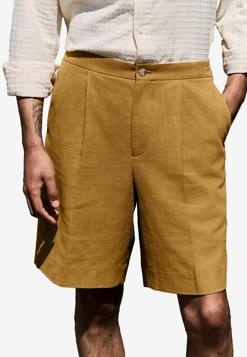 Sennepsfarvede linnedshorts med lige pasform, der har to sidelommer og en knaplukning i taljen. Struktureret stof.