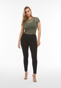 Oliivinvihreä ribbikuvioinen bodysuit, jossa on lyhyet hihat, yhdistetty korkeavyötäröisiin mustiin legginsseihin. Rakenne on tekstuuri, ja muotoilu on tiukka.