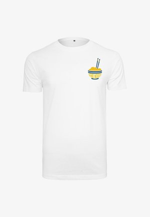 Homme debout portant un T-shirt blanc avec un petit motif bol et baguettes, pantalon cargo noir et baskets blanches sur un fond uni.