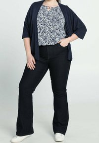 Marinblå cardigan över en vit och marinblå topp med swirl-mönster, i kombination med mörka utsvängda jeans och vita sneakers. Avslappnad och bekväm outfit.