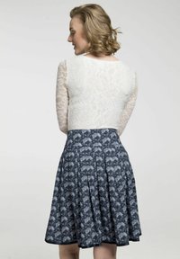 Spitzenoberteil mit langen Ärmeln und rundem Halsausschnitt, kombiniert mit einem blauen Faltenrock mit einem floralen Muster in Grau- und Weißtönen.
