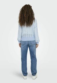 Maglione lavorato a maglia di un blu chiaro con un motivo a zigzag, abbinato a jeans blu sbiaditi e scarpe da ginnastica bianche. Il maglione presenta un bordo e polsini a coste.