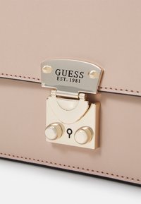 Rosa läderhandväska med ett guldmetalliskt lås med logotyp, rundat lås och två dekorativa knappar. Sytt detalj längs kanterna.
