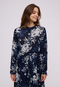 Robe à imprimé floral en marine, dotée de manches longues, d'une ceinture à la taille et d'un col rond. Le tissu est doux avec une texture lisse.