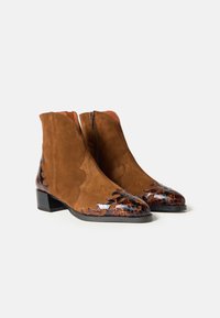 Bocanci maro din suede pentru glezne, cu toc mic, fermoare pe lateral și detalii din piele texturată maro închis la vârfuri și călcâie.