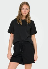 Schwarzes kurzärmeliges T-Shirt mit Rundhalsausschnitt und kleinem Logo auf der Brust, kombiniert mit schwarzen Shorts mit Kordelzug für einen abgestimmten Look.