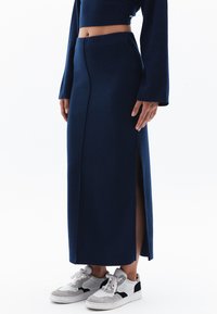 Navyblauwe, mid-length rok gemaakt van zachte stof met een zijsplit. Gekleed met witte sneakers met zwarte en grijze accenten.