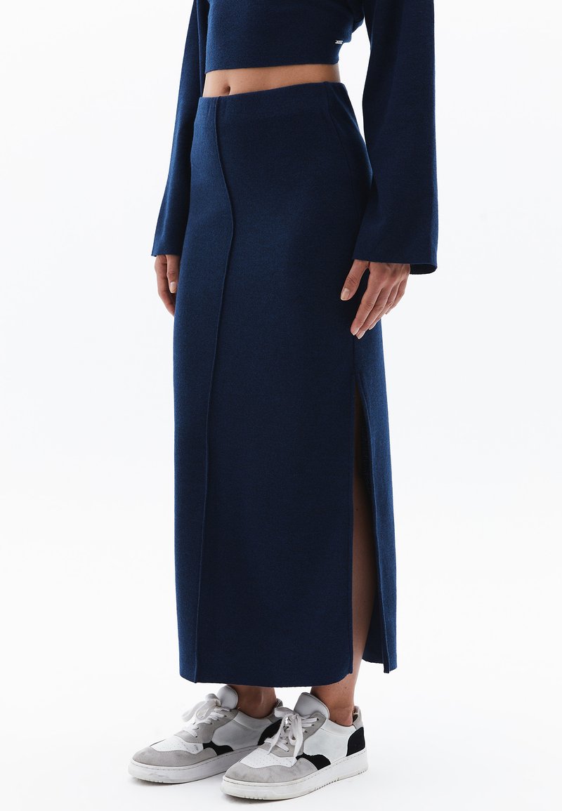 Navyblauwe, mid-length rok gemaakt van zachte stof met een zijsplit. Gekleed met witte sneakers met zwarte en grijze accenten.
