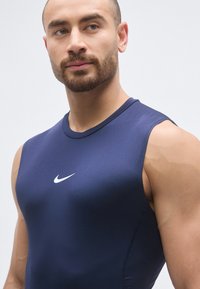 Top sportivo senza maniche color blu navy realizzato in materiale elastico con un logo Nike bianco al centro; texture liscia con design aderente.