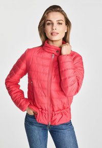 Różowa kurtka ocieplana z wysokim kołnierzem, zapinana na zamek błyskawiczny, z poziomym przeszyciem. Ma boczne kieszenie i dopasowaną talię.