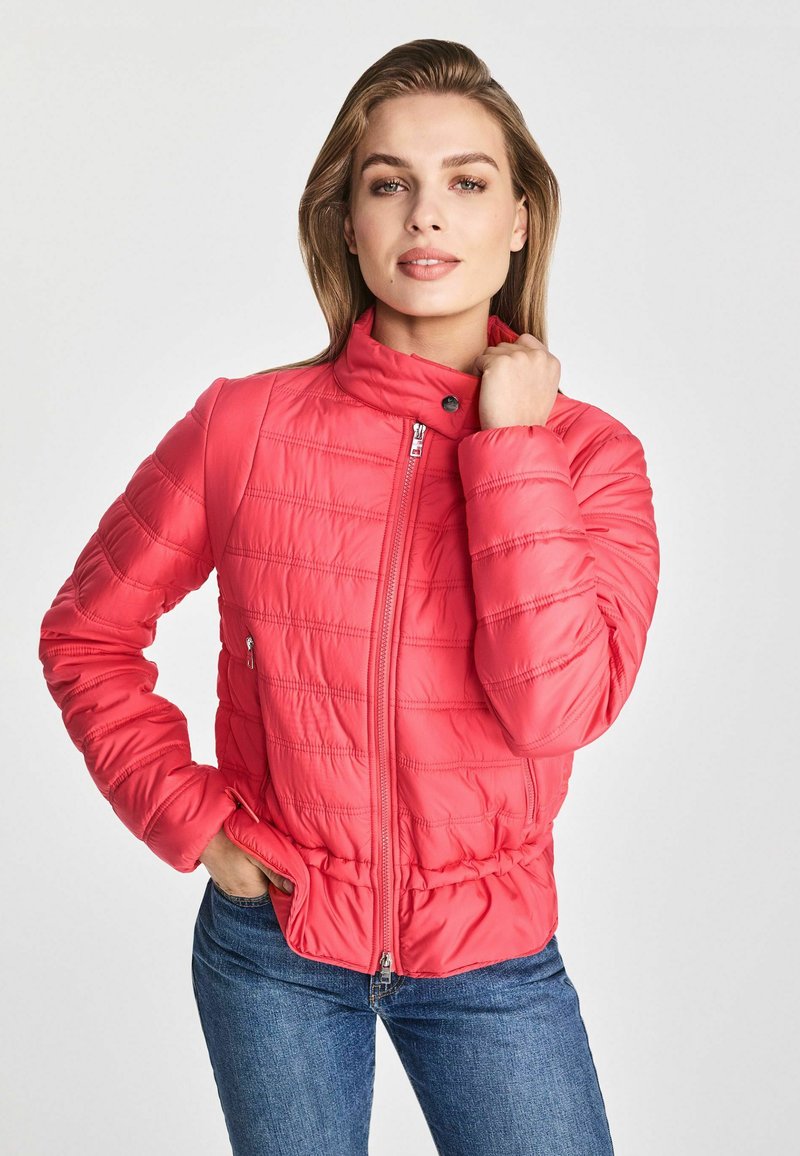Różowa kurtka ocieplana z wysokim kołnierzem, zapinana na zamek błyskawiczny, z poziomym przeszyciem. Ma boczne kieszenie i dopasowaną talię.