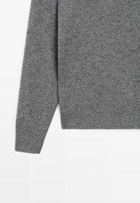 Pull en tricot gris avec un col rond, des poignets et un ourlet côtelés. Texture douce avec une finition lisse, idéale pour le superposé.