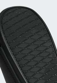 Black slip-on shoe featuring a textured rubber sole with a diamond pattern, smooth synthetic upper, and a cushioned footbed.