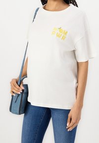 Vit bomull t-shirt med "MOM PWR" i gul brodyr och en liten citronaccent på bröstet. Kombineras med en blå handväska och jeans.