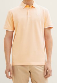 Ljus orange polo tröja med randig krage, två knappar, korta ärmar och textil med struktur. Bärs med beige byxor.