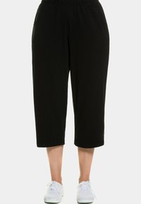 Schwarze, kurze Hosen aus weichem Stoff, mit elastischem Bund und seitlichen Taschen. Tragen sie mit weißen Turnschuhen.