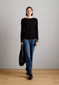 Schwarzer Langarmpullover, blaue gerade Jeans, schwarze Schuhe und eine schwarze Tragetasche. Einfaches Design auf hellem Hintergrund.