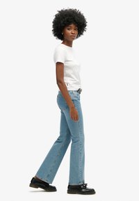 Camiseta ajustada blanca y jeans rectos de mezclilla azul claro. Los jeans tienen una textura clásica de mezclilla y un acabado ligeramente descolorido. Unos zapatos negros completan el look.
