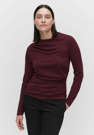Haut bordeaux à manches longues avec un col drapé et un tissu lisse et extensible. Porté avec un pantalon noir, il présente une silhouette ajustée.