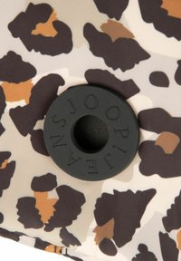 Il tessuto a stampa leopardata presenta sfumature di marrone, sabbia e beige. Un accento circolare in gomma nera con la scritta "JOOP!" è posizionato al centro.