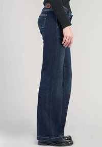 Breda blå denimjeans med medelhög midja, femficksdesign och kontrasterande sömmar. Slät textur med minimal hårdvaruaccent.