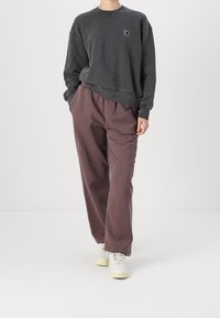 Grijze sweatshirt met een ronde hals en klein logo. Loszittende, bruine broek met een elastische tailleband. Witte sneakers.