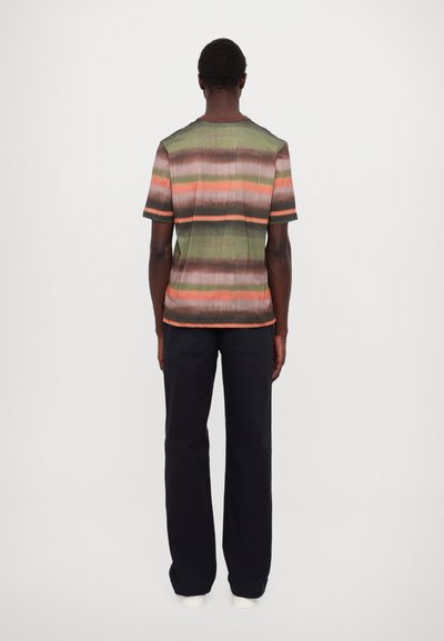 Striped short-sleeve shirt featuring green, orange, and black patterns, with a ribbed texture and straight hem. Paired with dark pants.