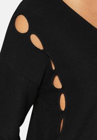 Schwarzes Stricktop mit asymmetrischem Ausschnitt und Aussparungen an den Ärmeln, die einen Kontrast zur darunterliegenden Haut bieten.