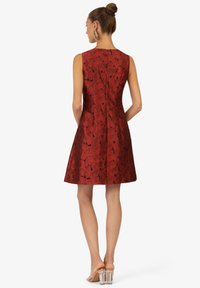 Rotes ärmelloses Kleid mit floralem Muster, tailliertem Oberteil, schwingendem Rock und strukturiertem Stoff. Verfügt über einen Reißverschluss auf der Rückseite und eine glatte Oberfläche.